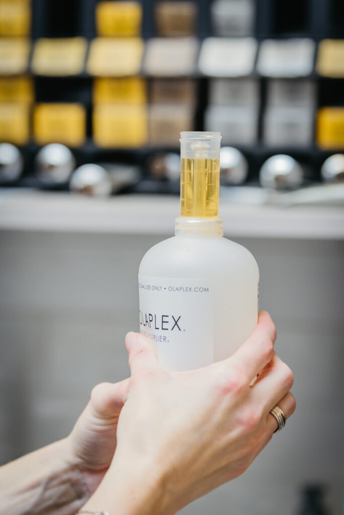 Olaplex fles vastgehouden door vrouwelijke handen, achtergrond blur